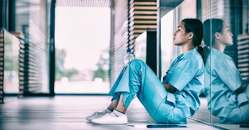 Exhausted nurse sitting down leaning against wall